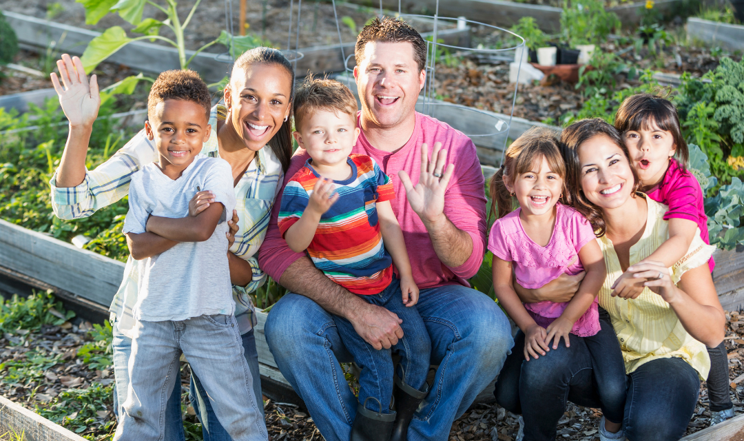 Adults and children smile and wave at the camera in a garden