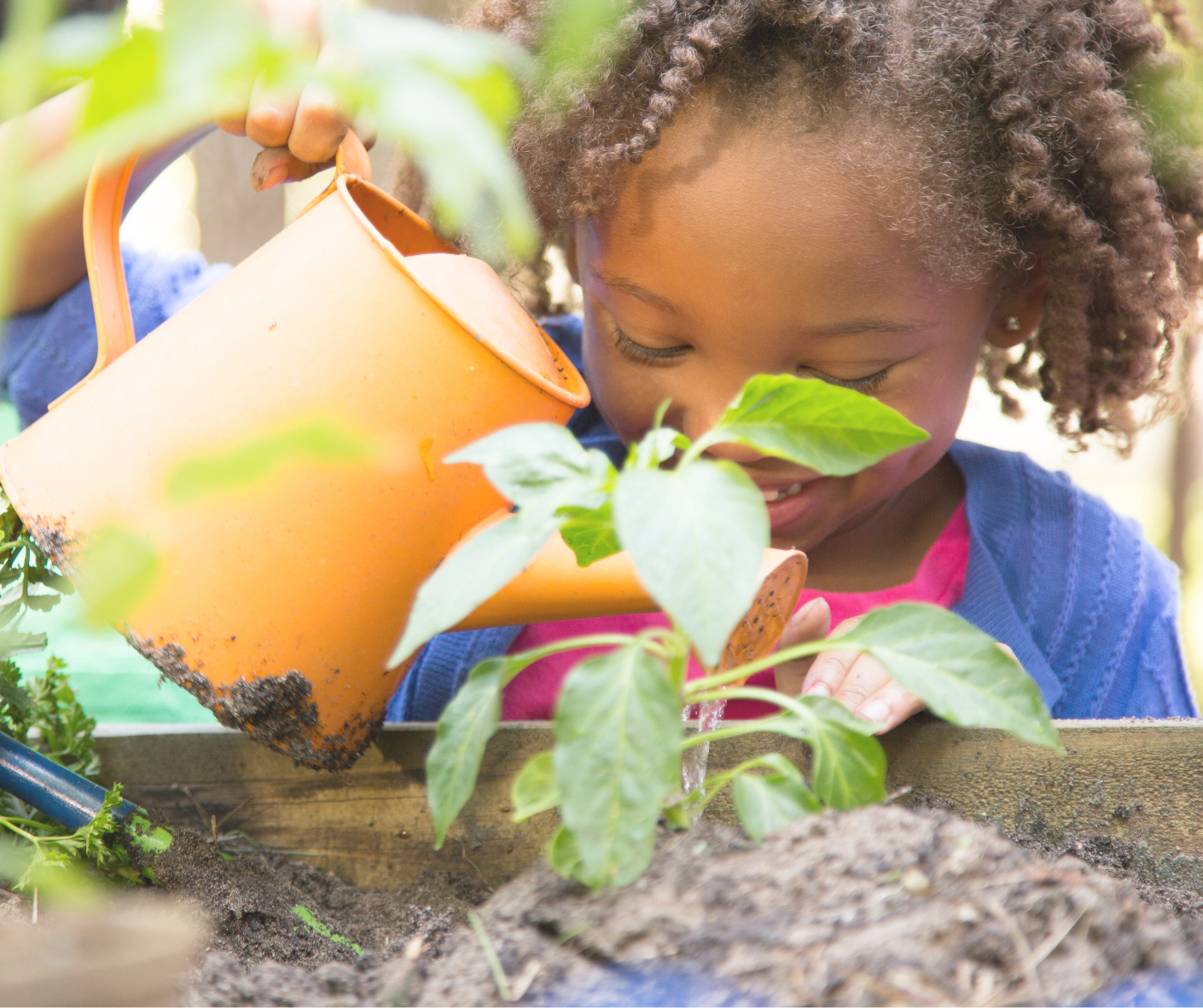 young child smiling and watering garden in outdoor classroom