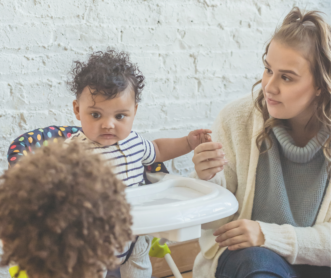 child care provider sitting next to a baby in a highchair