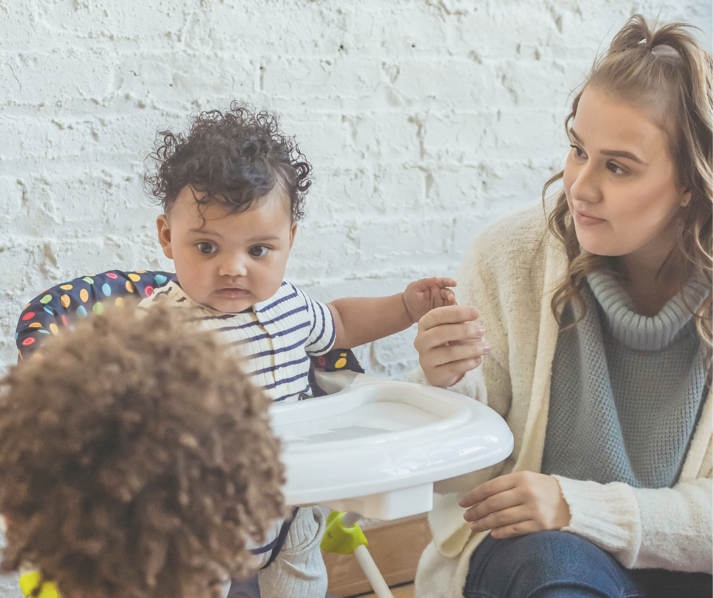 child care provider sitting next to a baby in a highchair 