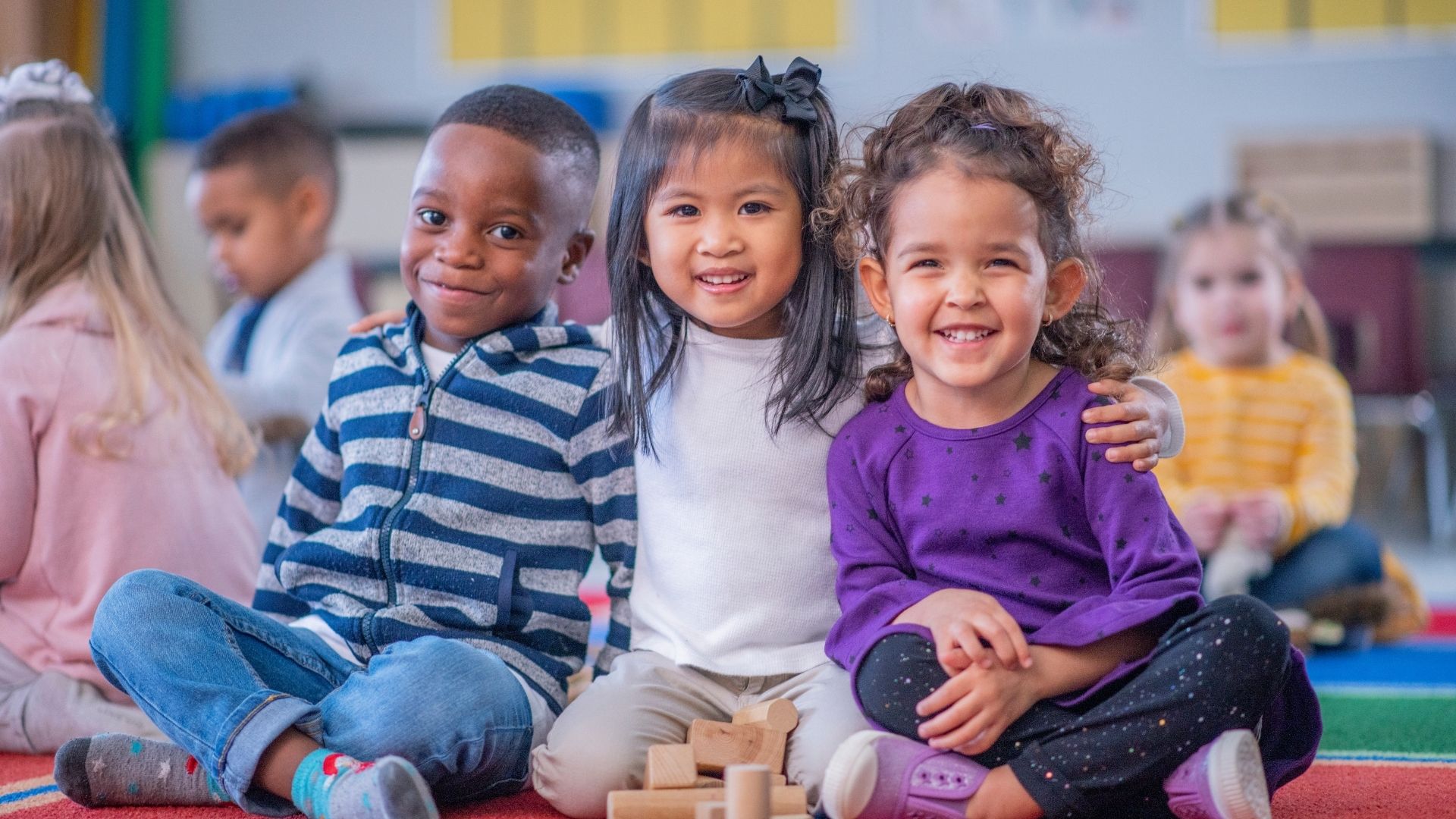 Stock image of three small children, smiling at a center-based program