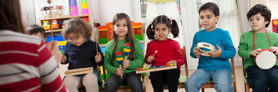 Teacher addresses five young children who are playing basic musical instruments