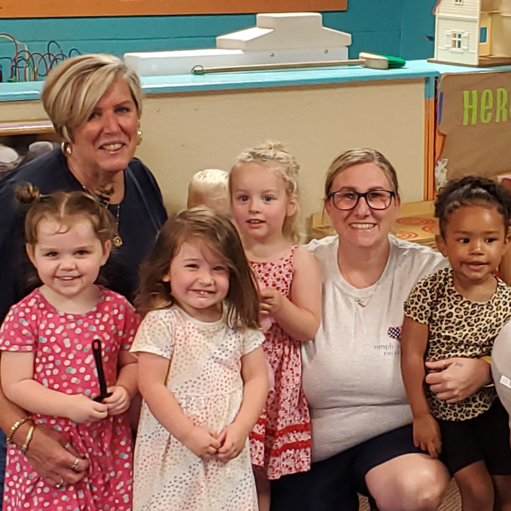 Two teachers and four young children pose in front of equipment in a classroom.