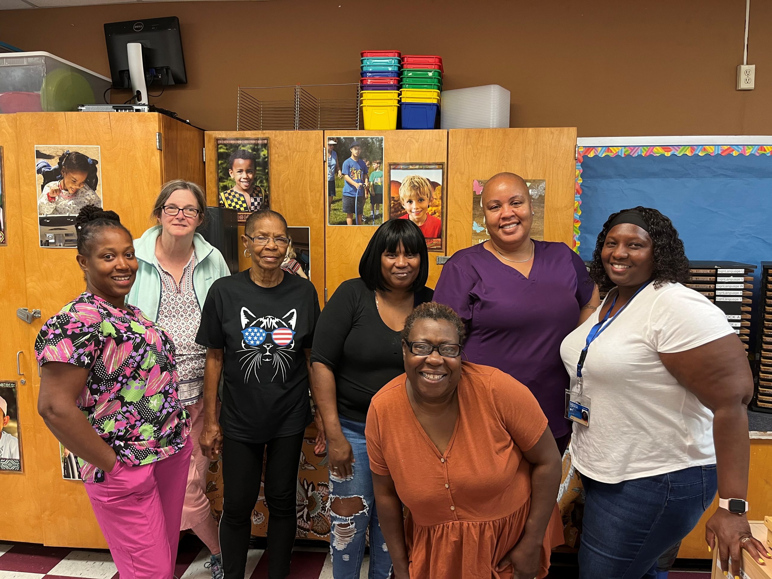 Group of teachers poses in a classroom in front of storage closets