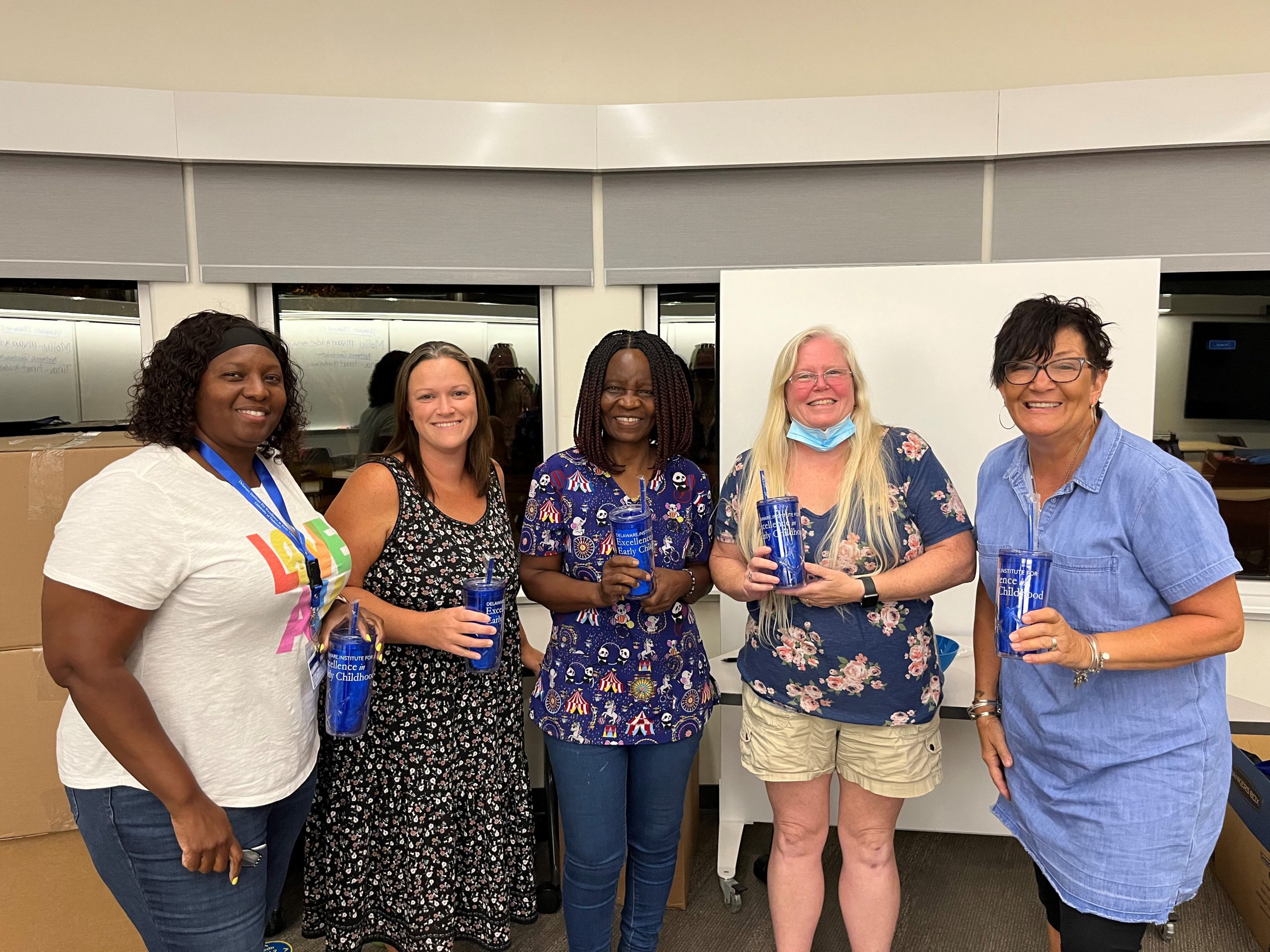 Five people pose with cups given away at the First State Family Child Care Conference