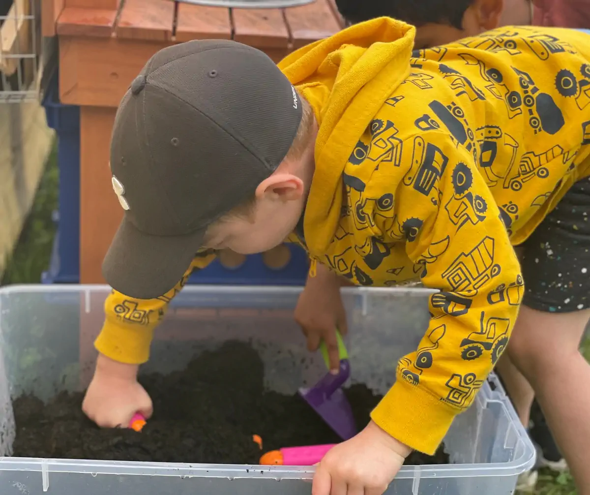 Child prepares dirt for planting in an outdoor classroom.