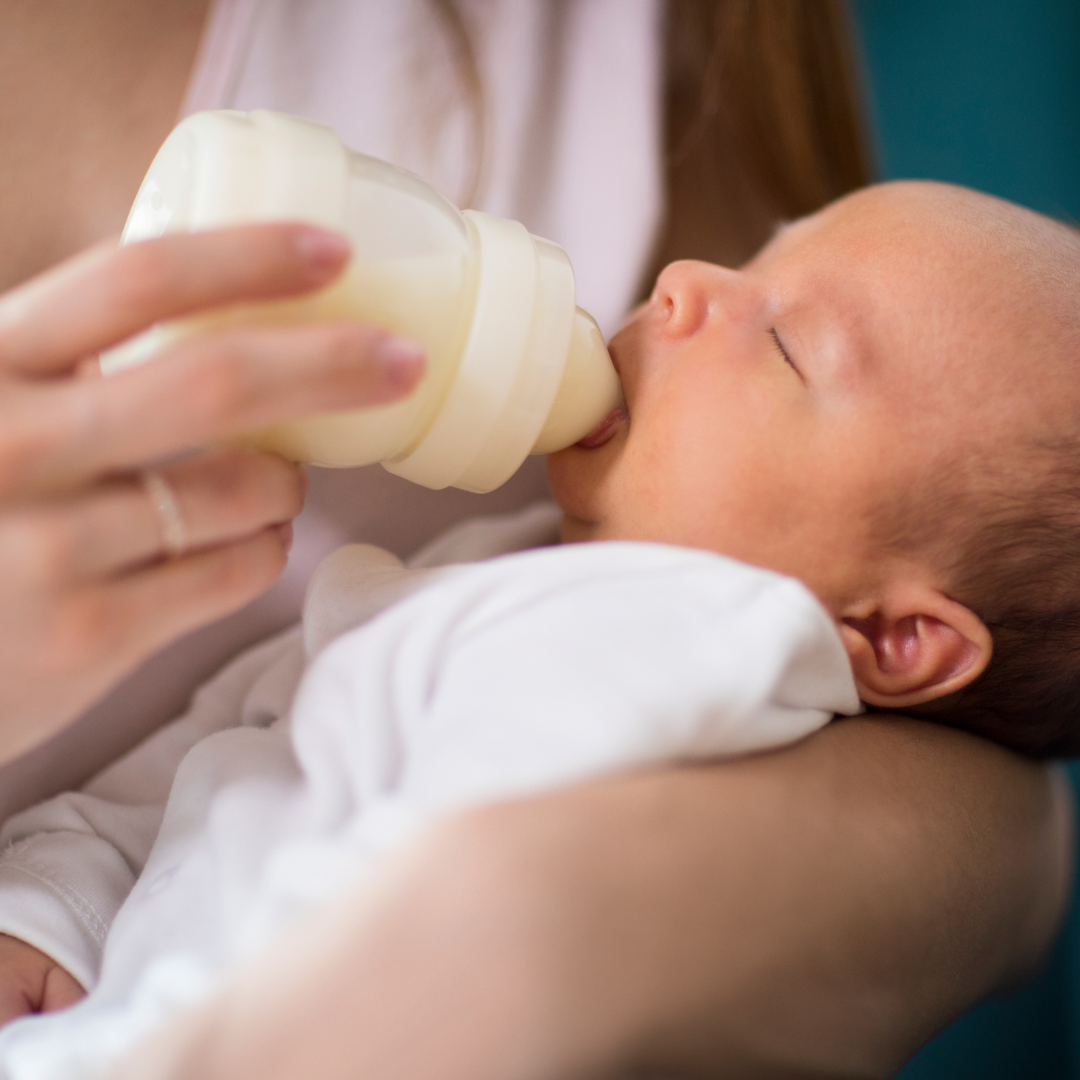 An adult gently feeds formula to an infant, demonstrating safe and responsive feeding practices.
